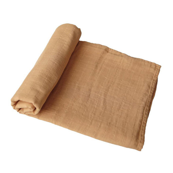 A rolled and partially unrolled muslin blanket in a warm autumn yellow color, displayed on a clean white background.