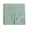 A green muslin cotton baby swaddle blanket folded on a white background.