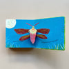 An open page of a bug-themed pop-up book showing a moth pop-up in the moonlight. The book is sitting open against a neutral background.