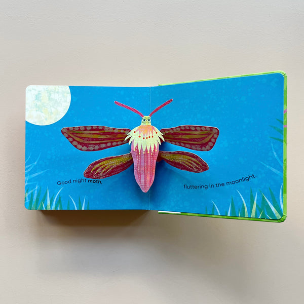 An open page of a bug-themed pop-up book showing a moth pop-up in the moonlight. The book is sitting open against a neutral background.