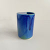 A small ceramic to-go cup featuring a vibrant blue glaze with subtle pops of green photographed against a neutral backdrop.