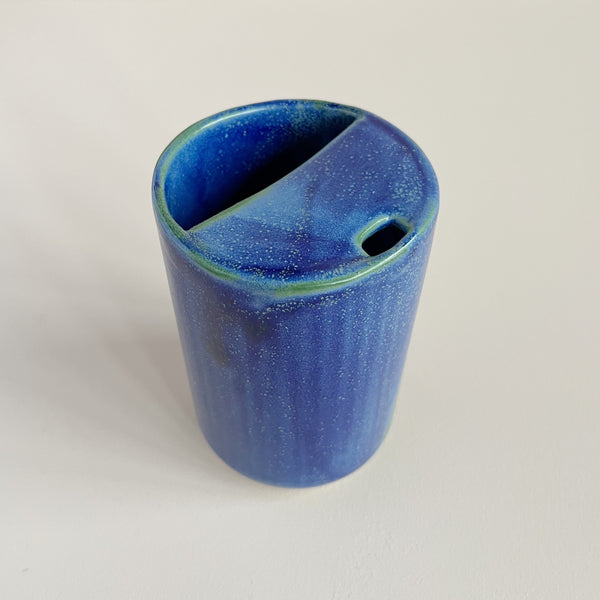 Top-down view of a small ceramic to-go cup featuring a vibrant blue glaze with subtle pops of green photographed against a neutral backdrop.