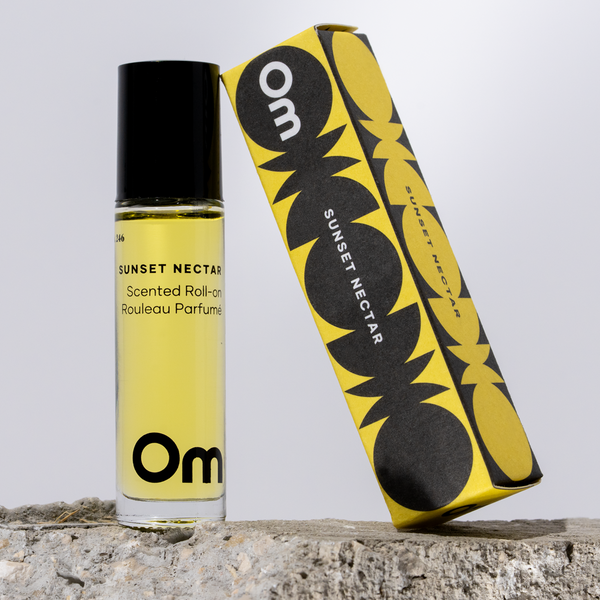 Perfume roll-on bottle and packaging with 'Om' branding on a light gray background