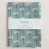 Linen tea towel with blue floral pattern and 'Our Heiday' branding on a light beige background