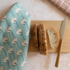 Bread slices on a wooden cutting board with a floral towel and knife on a light surface