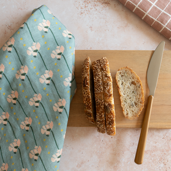 Bread slices on a wooden cutting board with a floral towel and knife on a light surface