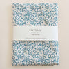Packaged linen tea towel with teal blue floral pattern on a beige background