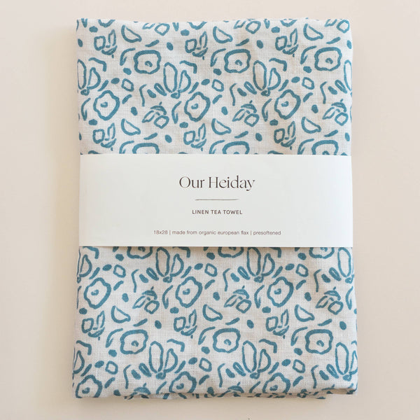 Packaged linen tea towel with teal blue floral pattern on a beige background