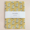 Yellow linen tea towel with floral pattern and 'Our Heiday' label on a beige background