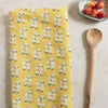 Yellow floral patterned towel on a light surface with a wooden spoon and small bowl of cherries.
