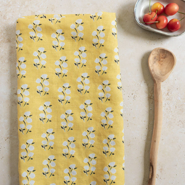 Yellow floral patterned towel on a light surface with a wooden spoon and small bowl of cherries.