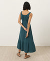Woman wearing a teal dress facing away toward the wall with a plain background
