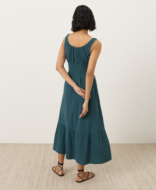 Woman wearing a teal dress facing away toward the wall with a plain background
