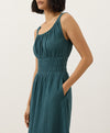 Woman wearing a teal dress with her hand in the side pocket against a white background