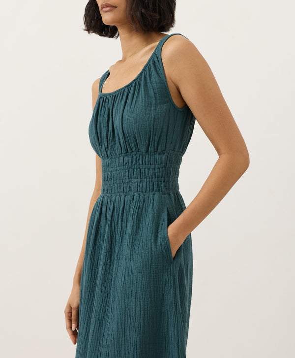 Woman wearing a teal dress with her hand in the side pocket against a white background