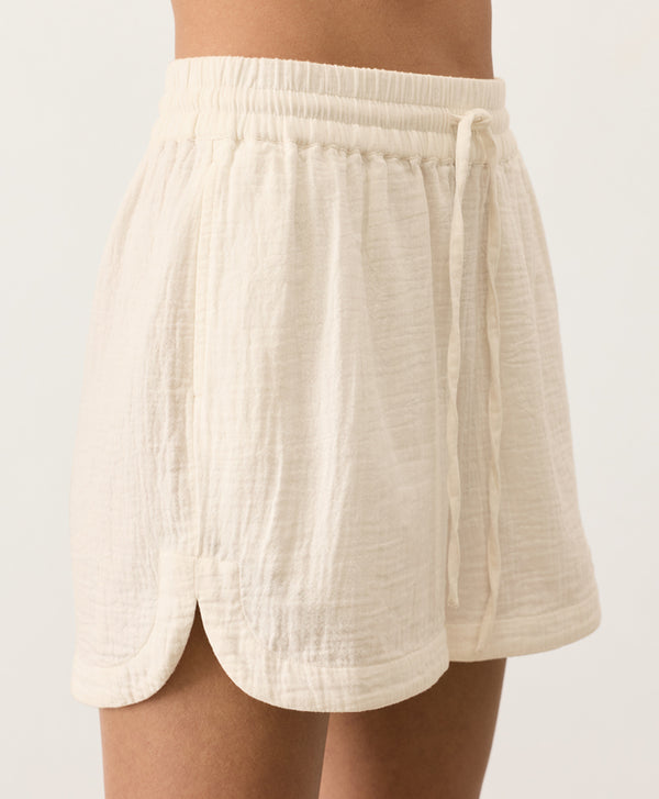 Cream shorts with a drawstring and curved hem on a light gray background