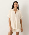 Woman wearing a cream button-up shirt and shorts on a white background