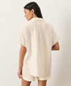 Woman wearing a cream short-sleeve shirt facing away against a white background
