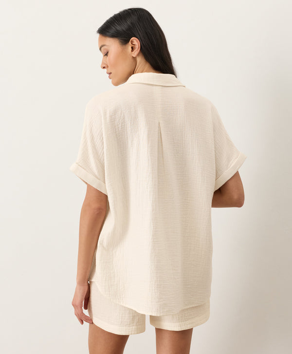 Woman wearing a cream short-sleeve shirt facing away against a white background