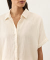 Woman wearing a cream short-sleeve shirt against a white background