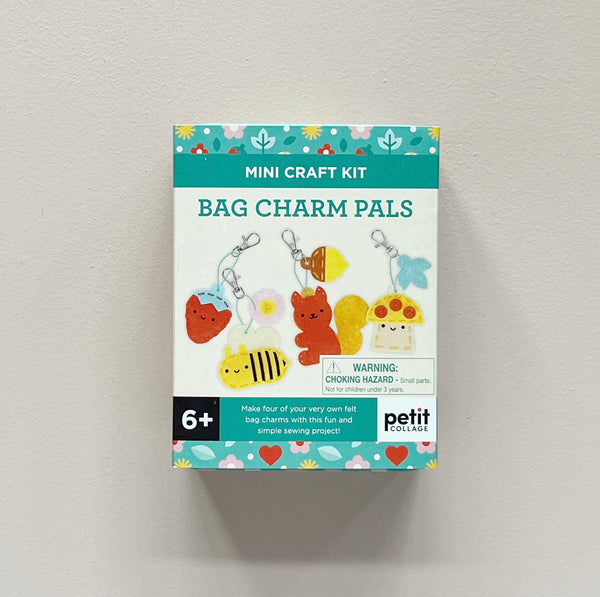 A boxed mini craft kit labeled 'Mini Craft Kit Bag Charm Pals' by Petit Collage, shown against a plain light wall. The package features colorful illustrations of bag charms including a red strawberry, yellow bee, brown bear, mushroom, and flower, with a black '6+' age mark and a choking hazard warning.