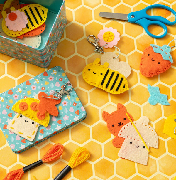 A table with a yellow honeycomb print, laid out with a felt craft kit for bag charms, along with safety scissors, embroidery floss, and a kid-safe needle.