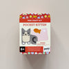 A Petit Collage 'Mini Craft Kit Pocket Kitten' in a square metal tin, mounted on a light beige wall. The packaging features a white center with illustrations of a gray and cream felt kitten and a pink felt fish, surrounded by a red top and bottom band with colorful patterned dots.