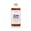 A bottle of Pink House Alchemy Creamy Salted Caramel syrup on a white background. The clear glass bottle shows the amber-brown syrup inside, with a white label featuring a simple house illustration and the brand name 'pink House ALCHEMY'.