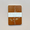 A small notebook featuring a warm caramel brown waxed paper cover featuring a design of pastel flowering tree with white packaging saying 'Ro-biki Note Shape Series' against a neutral background.