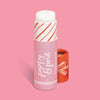 A pink lip balm tube labeled 'poppy & pout' and 'Candy Cane Fluff' with a white balm stick, shown next to its red cap on a solid pink background. There is a candy cane swirl on the tube revealed when the top comes off.