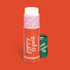 Lip balm with a red container a green lid set aside on a bright red backdrop.