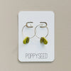 Gold hoop earrings with chartreuse clay and brass accents on a 'Poppyseed' branded card against a beige background
