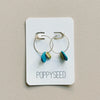 Pair of hoop earrings with blue and brass accents on a Poppyseed branded card.