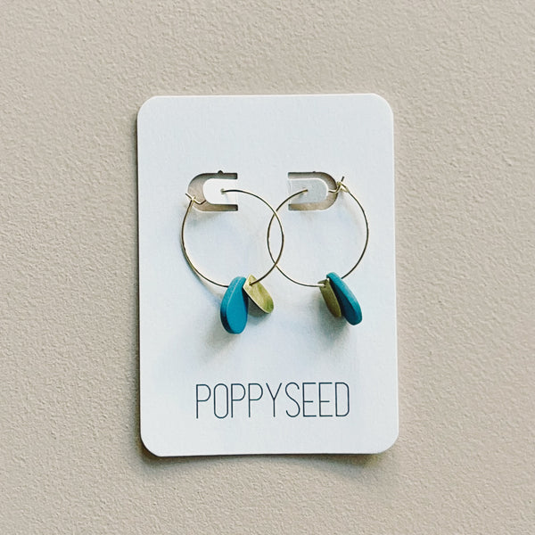 Pair of hoop earrings with blue and brass accents on a Poppyseed branded card.