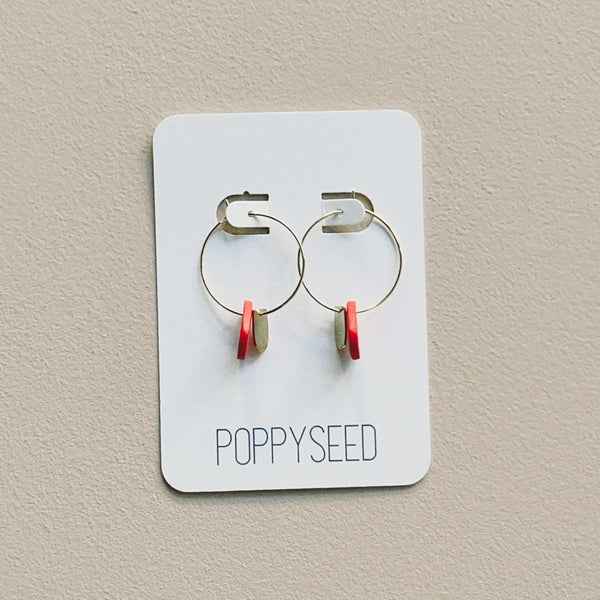 Pair of hoop earrings with red clay and brass accents on a 'Poppyseed' branded card against a beige background
