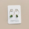 Gold hoop earrings with green clay and brass charms on a Poppyseed branded card.