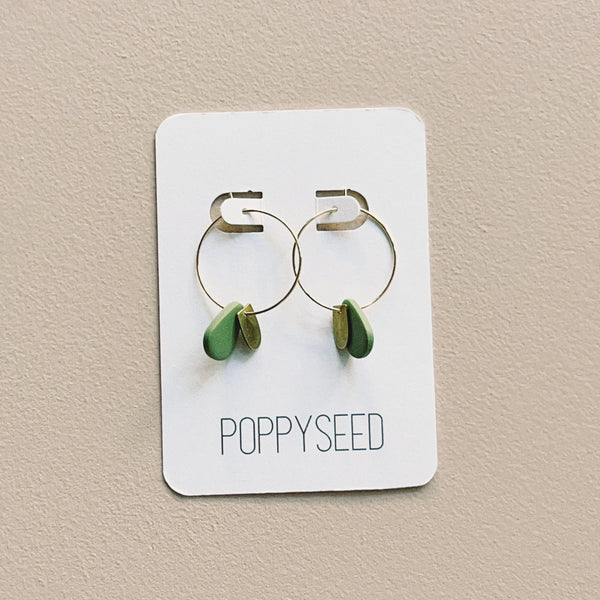 Gold hoop earrings with green clay and brass charms on a Poppyseed branded card.
