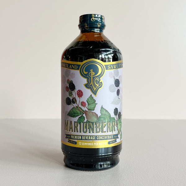 A bottle of Marionberry Premium Beverage Concentrate syrup, featuring a purple label with marionberry illustrations and a gold and blue logo, set against a plain light background.