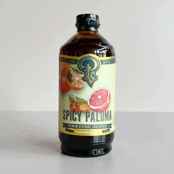 A bottle of Portland Syrup 'Spicy Paloma' premium beverage concentrate, featuring a cream-colored label with illustrations of citrus fruits, set against a plain light gray background.