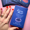 Blue card deck titled 'Deep Rest' held by a hand with red nail polish on a pink background