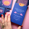 Blue card box with text and graphics held by a hand on a pink background