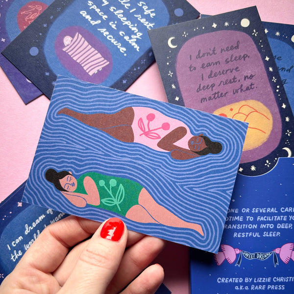 Card with illustration of two women lying on a wave held by a hand against a pink background. There are several other cards displayed in the background.