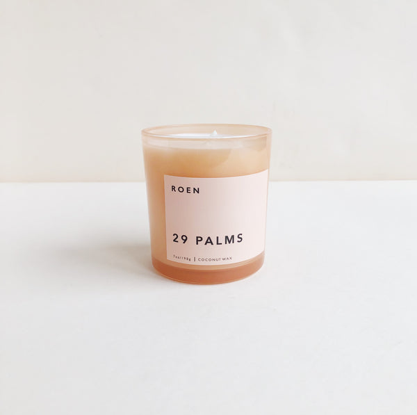 A pink glass jar candle labeled with 'Roen 29 Palms' against a beige background.