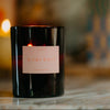 A brown glass jar candle with a pink label 'Roen Ojai Nuit' against a blurred background.