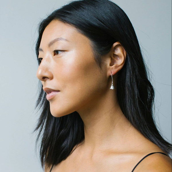Woman wearing a silver floral charm drop earring against a gray background