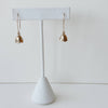 Pair of yellow bronze floral earrings on a white earring stand against a light gray background