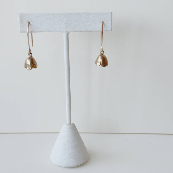 Pair of yellow bronze floral earrings on a white earring stand against a light gray background