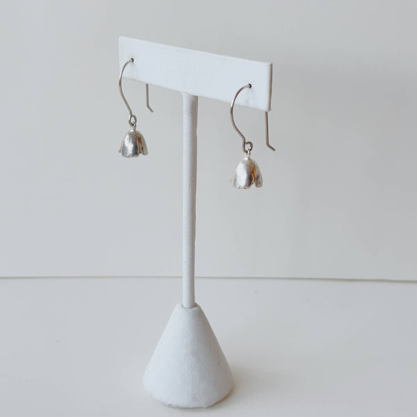 Silver flower shaped earrings on a white earring stand against a light gray background
