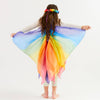 Child with long brown curly hair wearing a colorful rainbow wings and headband on a white background