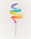 A rainbow silk streamer attached to a wood wand with a purple tip against a white backdrop.